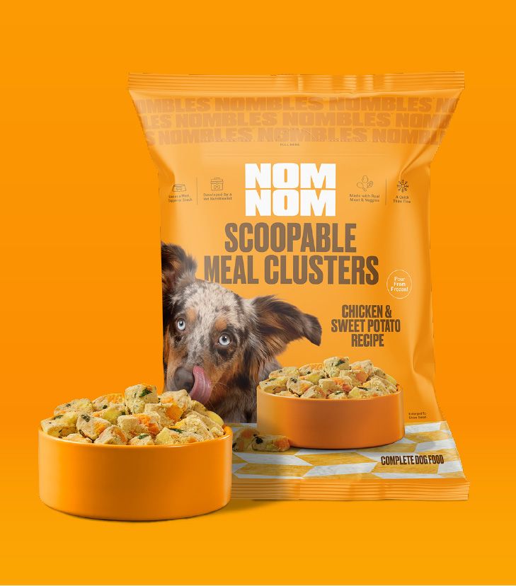 Nom Nom Scoopable Meal Clusters in bright orange packaging feature the Chicken &
Sweet Potato Recipe, with a blue-eyed, merle-coated dog pictured licking its nose.
The bag highlights that the clusters are complete dog food made with real ingredients.
Two orange bowls in front show scoopable, bite-sized clusters with visible vegetable pieces
on a clean orange background.