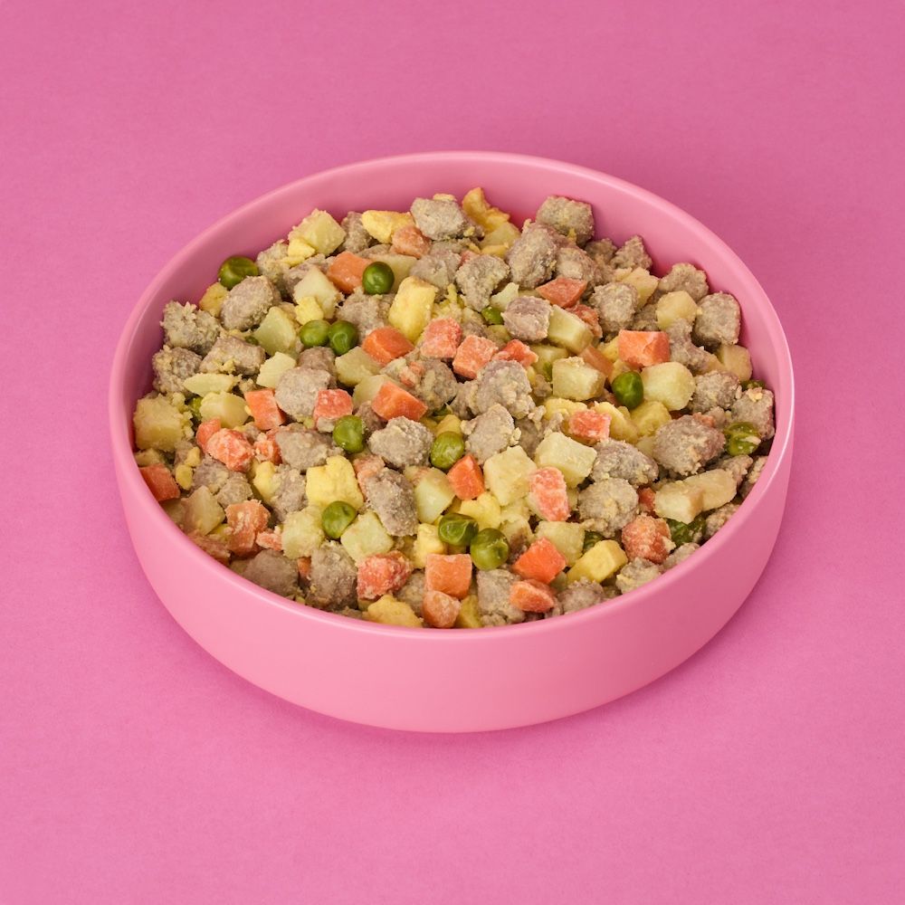 Pink bowl of Nom Nom dog food with a pink background