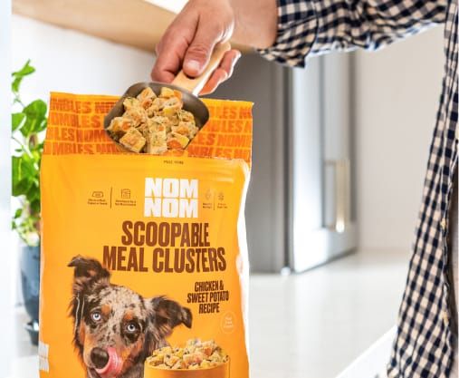 A hand scooping out Nom Nom Scoopable Meal Clusters from a bag